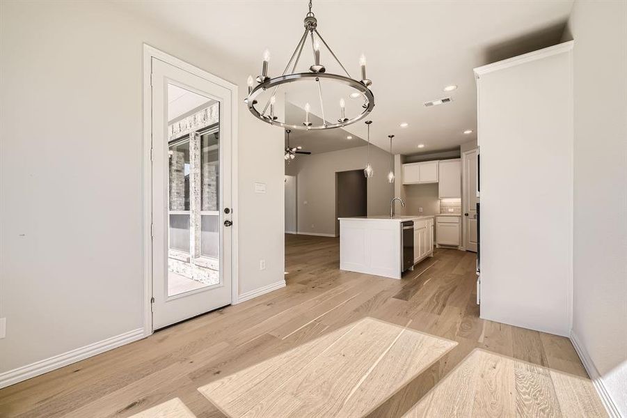 Kitchen with white cabinets, a center island with sink, pendant lighting, light hardwood / wood-style floors, and sink