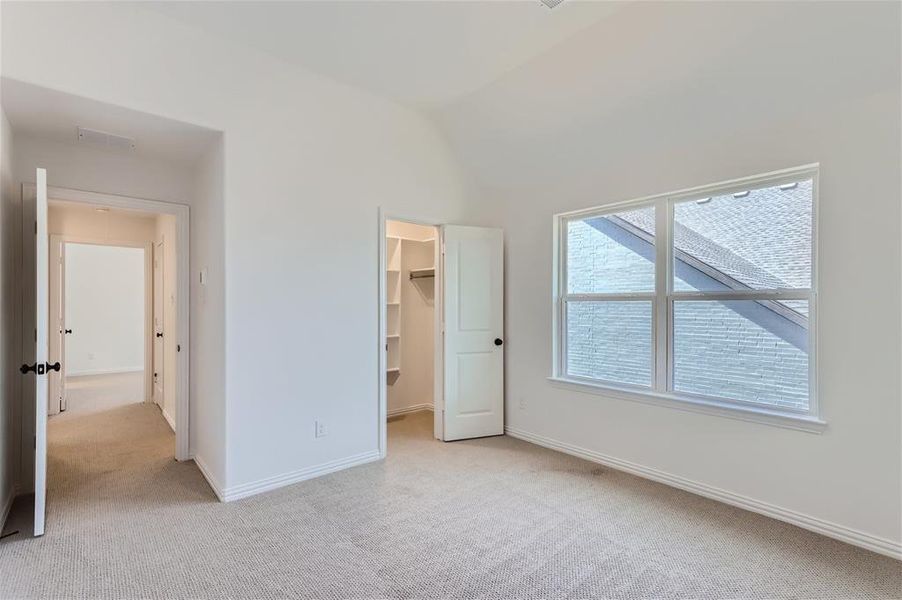 Unfurnished bedroom with light carpet, a walk in closet, lofted ceiling, and a closet