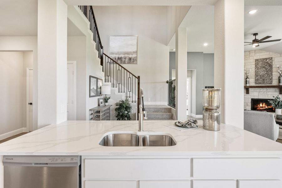 Kitchen island with quartz countertop and double sink overlooking open living area with staircase and fireplace