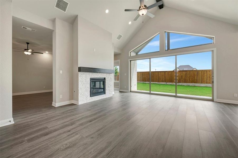 Vaulted ceiling living space with wood-finish flooring, a white brick fireplace with dark wood mantel, and expansive sliding glass doors opening to the backyard