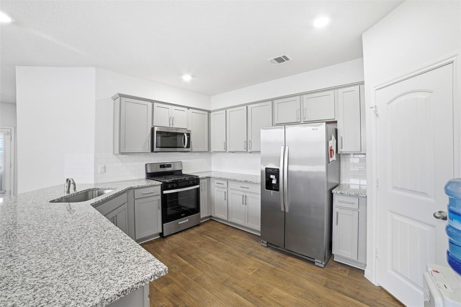 Kitchen featuring stainless steel appliances, light stone countertops, dark wood-style floors, and gray cabinetry Kitchen featuring stainless steel appliances, light stone countertops, dark wood-style floors, and gray cabinetry