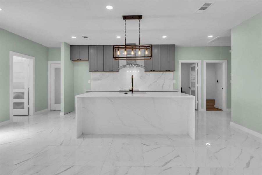 Kitchen with backsplash, recessed lighting, decorative light fixtures, a center island with sink, and light stone countertops Kitchen with backsplash, recessed lighting, decorative light fixtures, a center island with sink, and light stone countertops