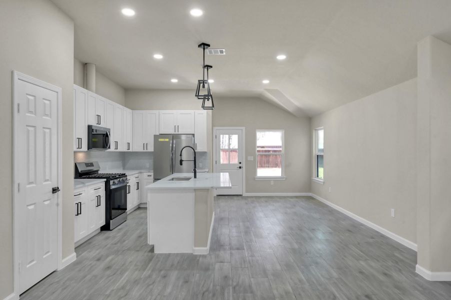 Spacious open-concept kitchen and dining area featuring sleek wood-look flooring, recessed lighting, and a modern island with breakfast bar seating.