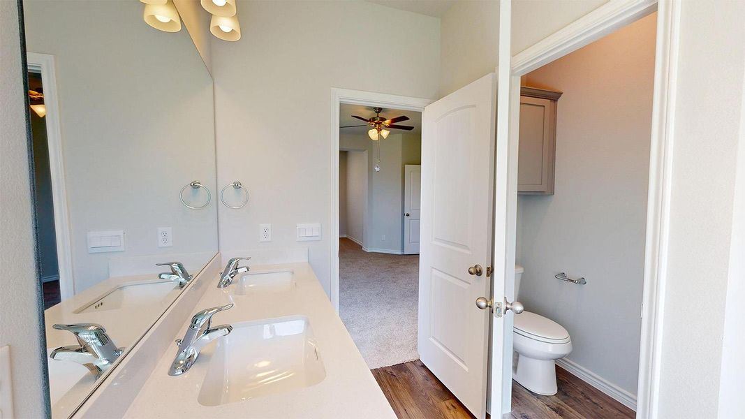 The bathroom features a double vanity with two sinks, wall-mounted light fixtures, and a private water closet with a toilet and cabinet