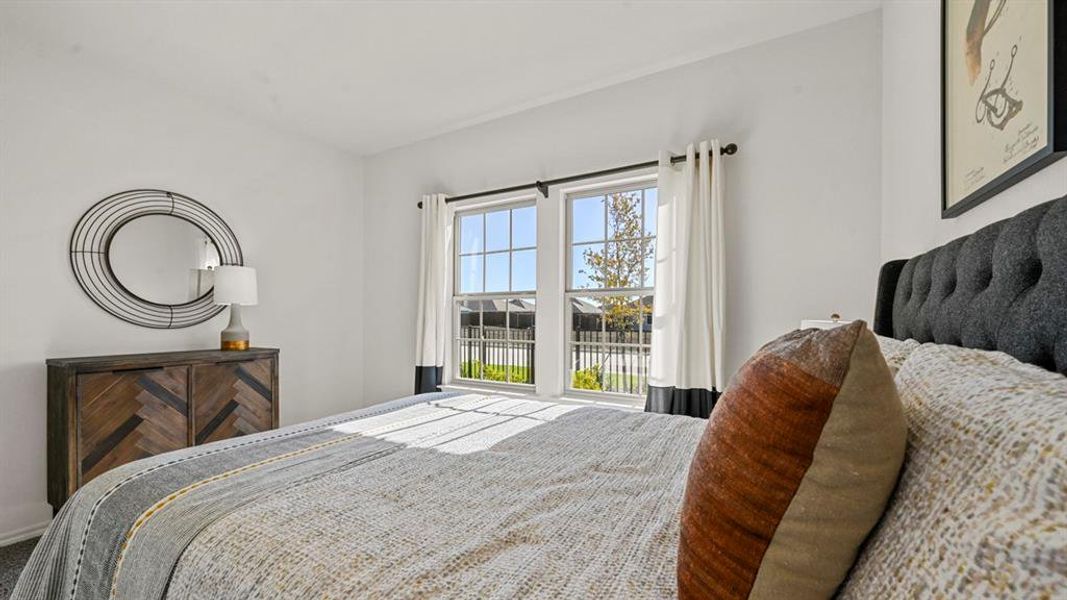 This room features bright white walls, a large window with white curtains, and a dark upholstered headboard This room features bright white walls, a large window with white curtains, and a dark upholstered headboard