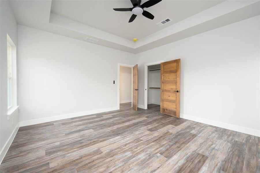 Unfurnished bedroom with a raised ceiling, ceiling fan, wood finished floors, and a walk in closet