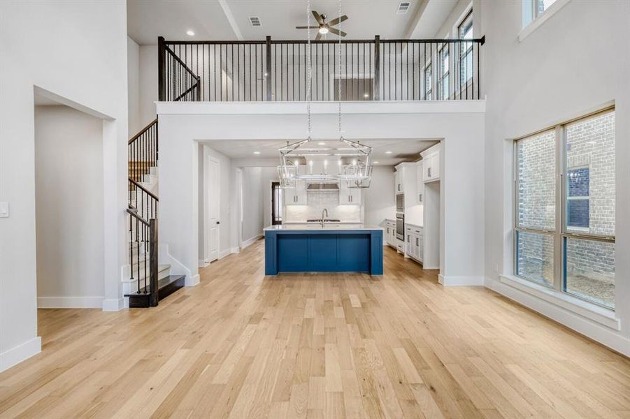 Kitchen featuring open floor plan, pendant lighting, light wood-type flooring, a spacious island, and a high ceiling