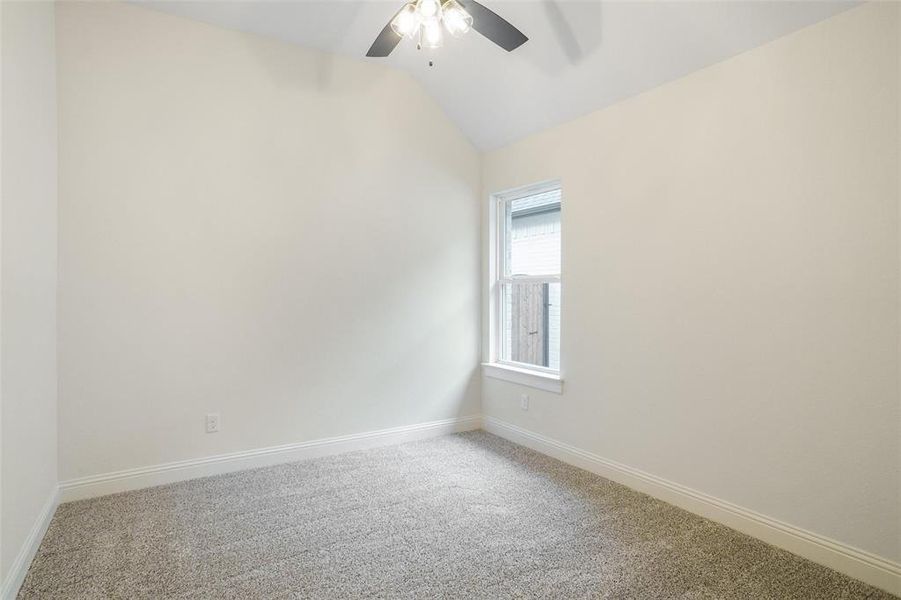 Carpeted empty room featuring ceiling fan and vaulted ceiling