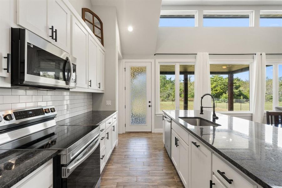 Kitchen with white cabinets, appliances with stainless steel finishes, sink, and dark stone counters