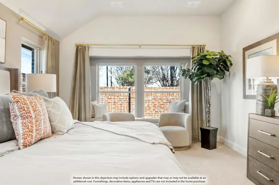Bedroom with vaulted ceiling, large windows, sitting area with two chairs, and neutral carpet flooring