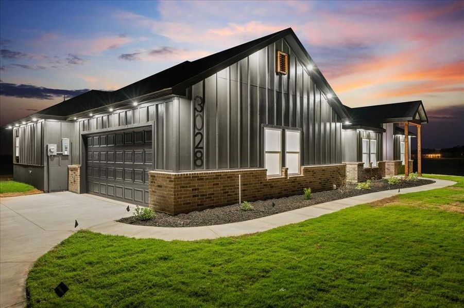 Modern farmhouse at dusk with siding, brick accents, bright exterior lighting, and great curb appeal.