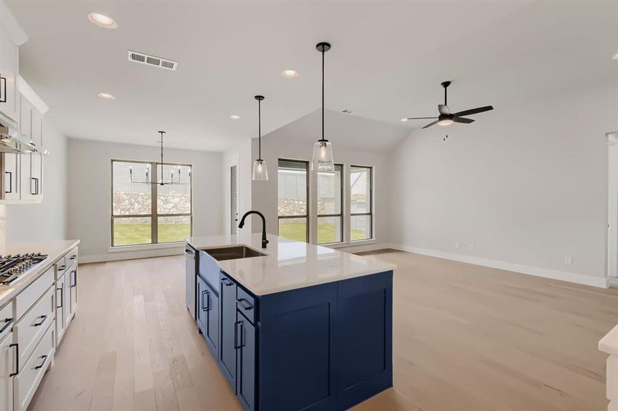 Kitchen island with a farmhouse sink and black faucet, white shaker cabinetry with black hardware, gas cooktop, recessed lighting, and wood-finish flooring throughout