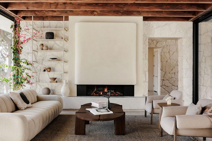 Etherial living room with exposed limestone walls, gas fireplace, curved, plaster hood and 4 floor-to-ceiling sliding glass doors to open up the space to the front and rear courtyards.