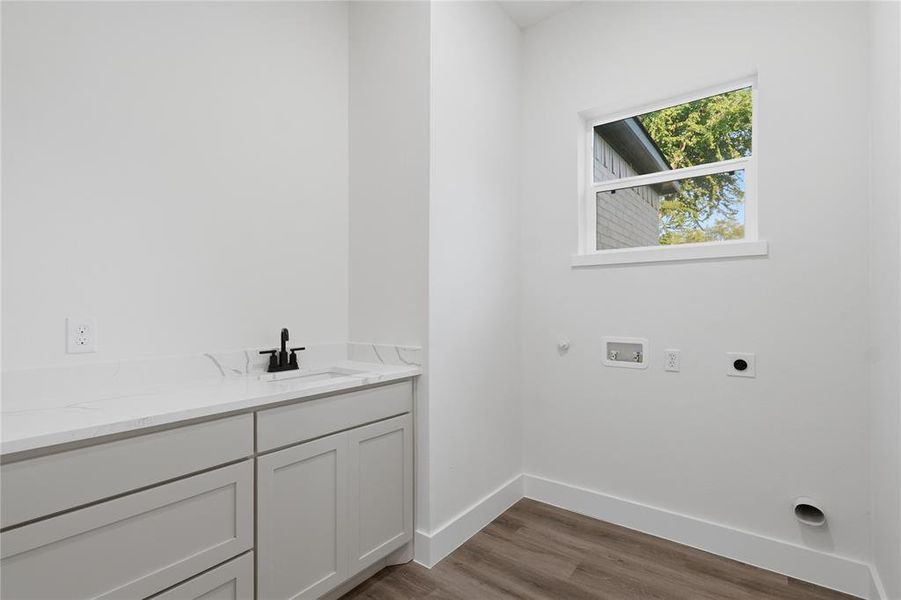 Utility room featuring light gray cabinetry with a white countertop, an undermount sink with a matte black faucet, and wood-finish flooring