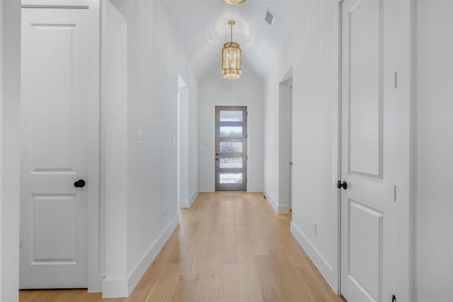 Corridor featuring light wood-style flooring, a barrel ceiling, and suspended lighting