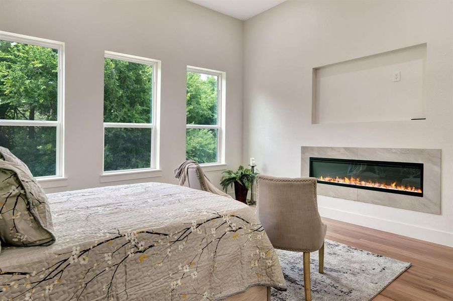 Room featuring a linear fireplace with a stone-look surround, three large windows, a high ceiling, and wood-finish flooring Room featuring a linear fireplace with a stone-look surround, three large windows, a high ceiling, and wood-finish flooring