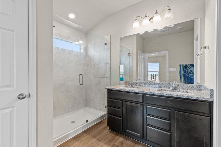 Bathroom with double vanity, a shower stall, wood finished floors, and recessed lighting