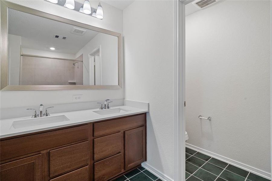 Another view of the primary bathroom featuring dark stained cabinets with light countertops, dual vanity space, custom paint, sleek and dark modern finishes.