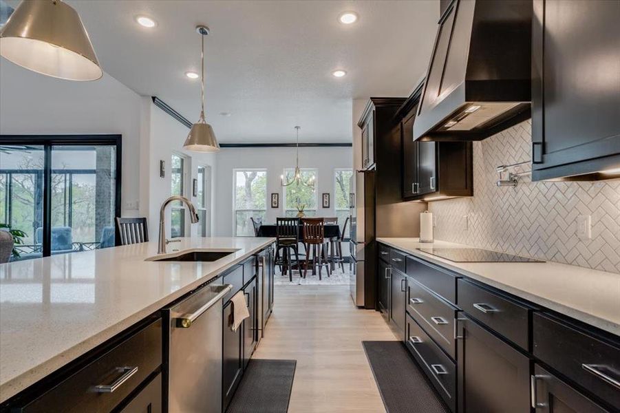 Kitchen with light stone countertops, stainless steel appliances, light wood-look tile floors, hanging light fixtures, and backsplash