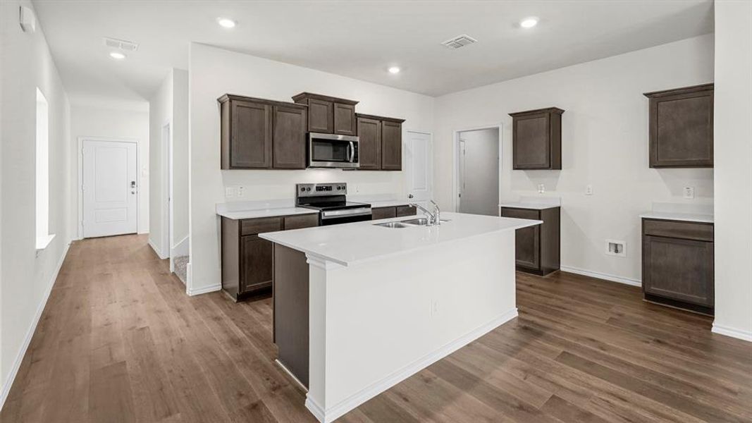 The kitchen features dark wood cabinetry, white countertops, a central island with a double sink, and stainless steel appliances including a microwave and range