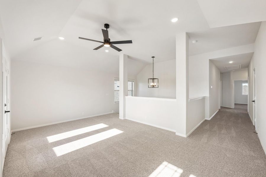 Open upstairs living area with vaulted ceiling, ceiling fan, carpet flooring, and hallway leading to additional rooms Open upstairs living area with vaulted ceiling, ceiling fan, carpet flooring, and hallway leading to additional rooms