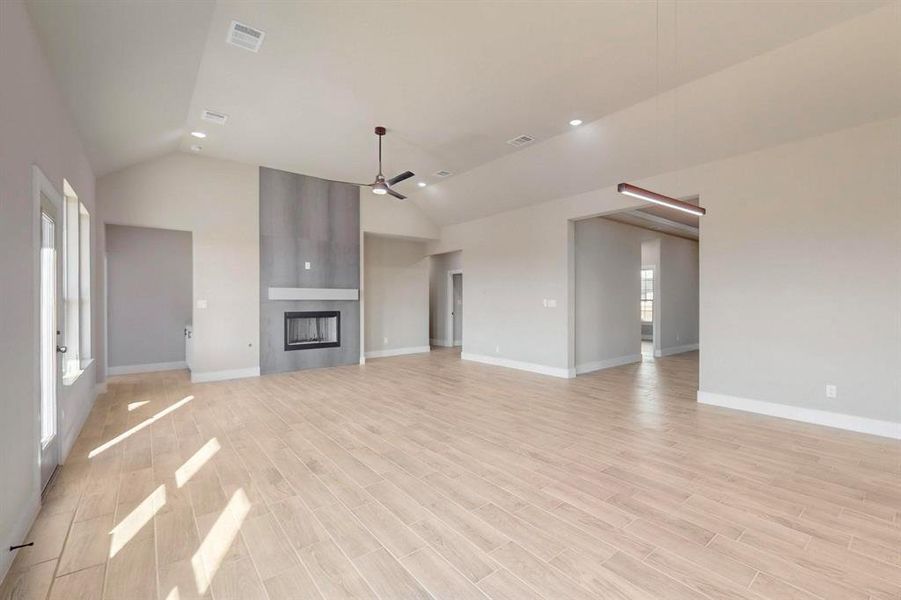 Unfurnished living room with visible vents, a large fireplace, baseboards, ceiling fan, and light wood-type flooring