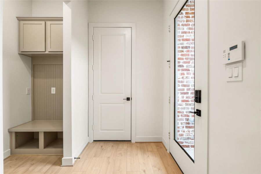Thoughtful mudroom drop zone — custom built-in bench seating, storage cubbies, upper cabinets, and glass-paneled front entry door.