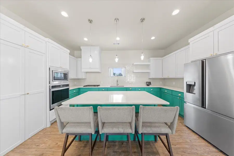 Kitchen featuring stainless steel appliances, a kitchen bar, a center island, white cabinetry, and light countertops Kitchen featuring stainless steel appliances, a kitchen bar, a center island, white cabinetry, and light countertops