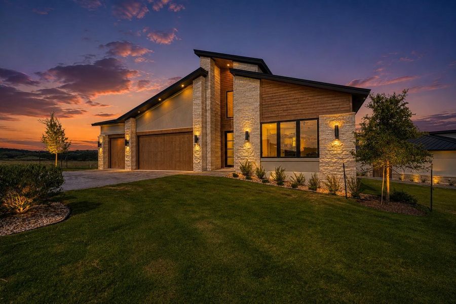 Dramatic rooflines and stone accents define this modern exterior under a sunset sky.