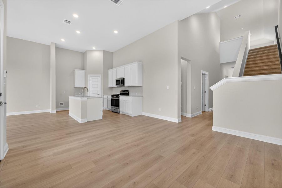 Unfurnished living room featuring a high ceiling, light wood-style floors, stairway, and recessed lighting