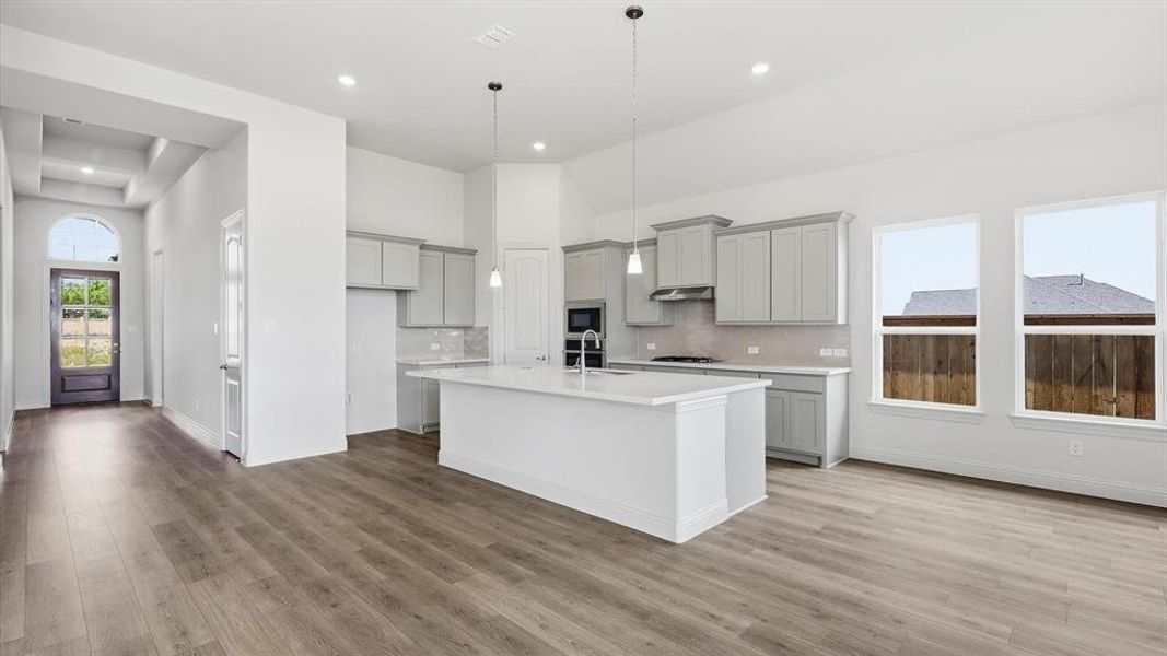 Open-concept living area featuring wood-finish flooring, a contemporary kitchen island with a white countertop, light gray cabinetry, recessed lighting, and large windows