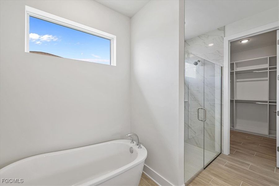 Full bath featuring a marble finish shower, a freestanding bath, a walk in closet, and wood tiled floors
