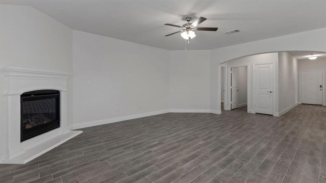 Unfurnished living room with a glass covered fireplace, wood tiled floors, arched walkways, and ceiling fan
