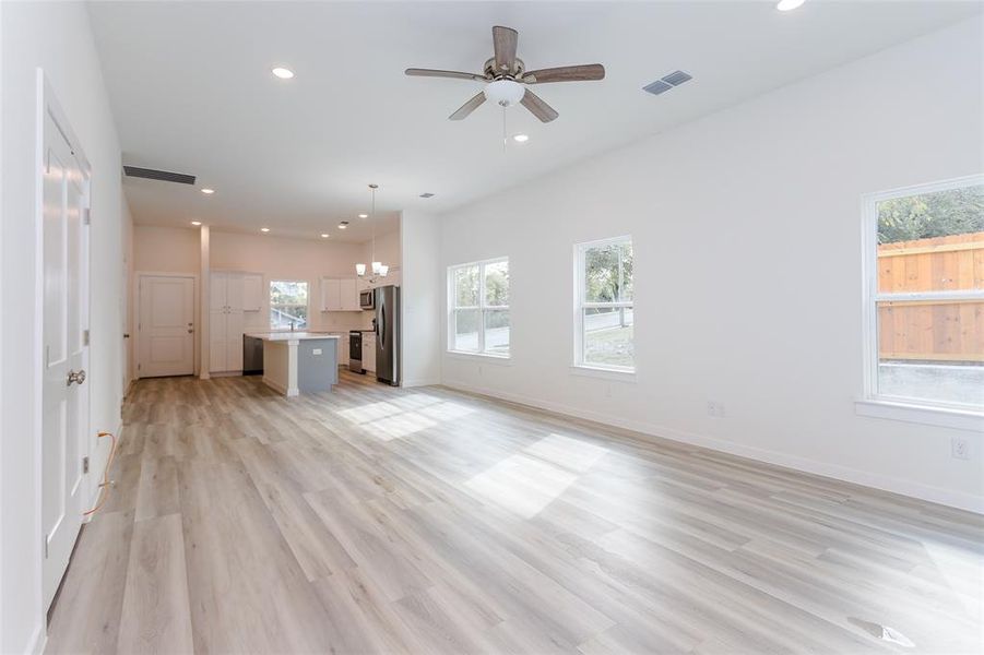 Unfurnished living room with light hardwood / wood-style floors and ceiling fan with notable chandelier