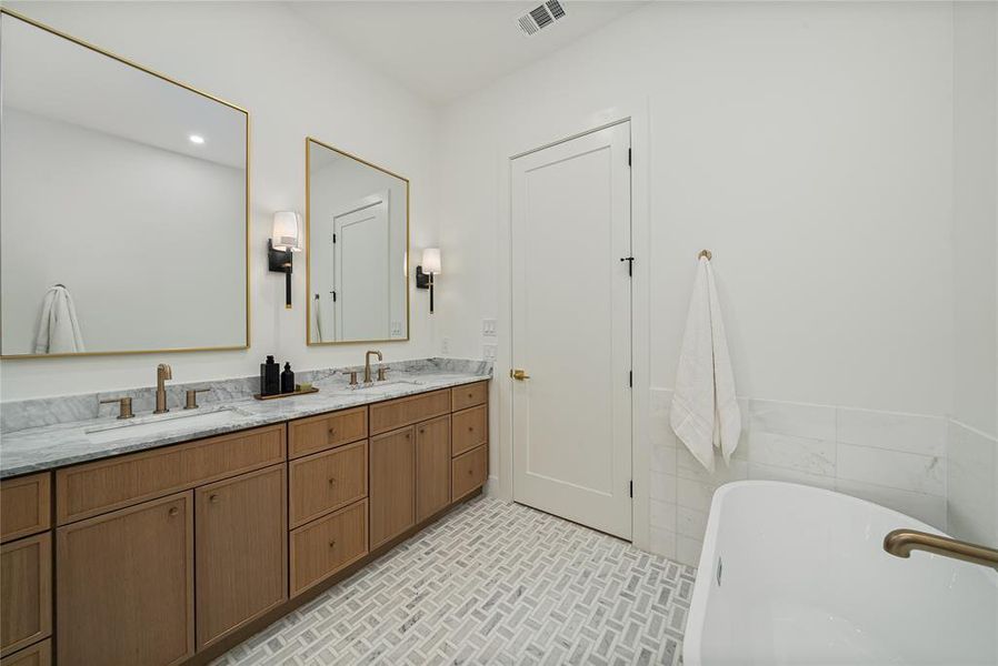 Well-appointed bathroom featuring a double vanity with ample storage, two gold-framed mirrors, and a white soaking tub