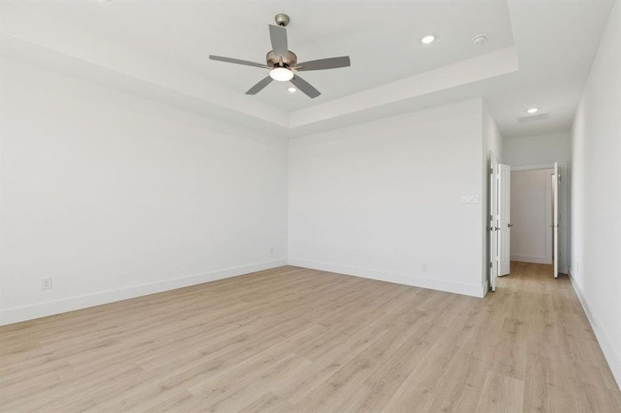 Unfurnished room with a raised ceiling, light wood-style flooring, recessed lighting, and a ceiling fan