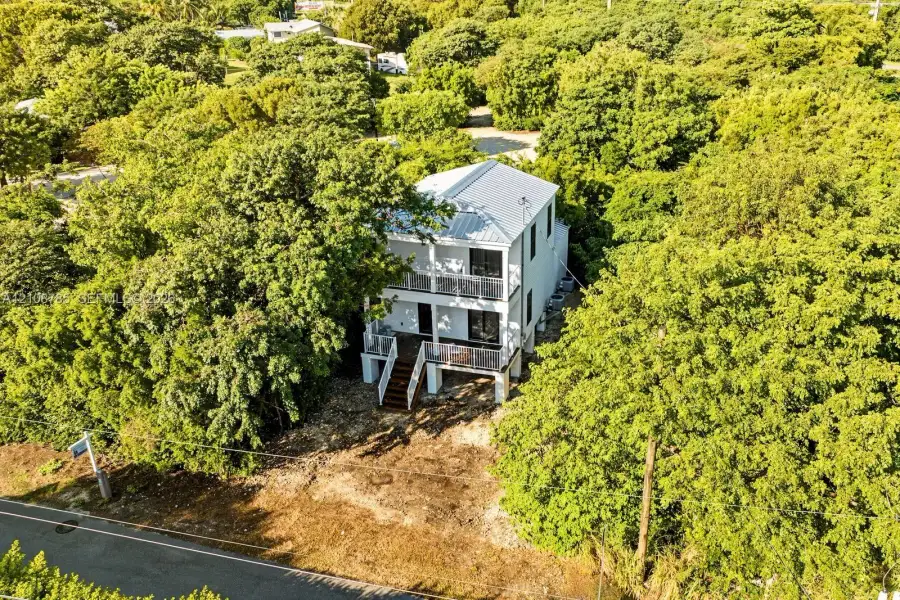 Two-story residence featuring a metal roof, stacked porches with metal railings, and elevated construction, situated on a lot with mature trees Two-story residence featuring a metal roof, stacked porches with metal railings, and elevated construction, situated on a lot with mature trees