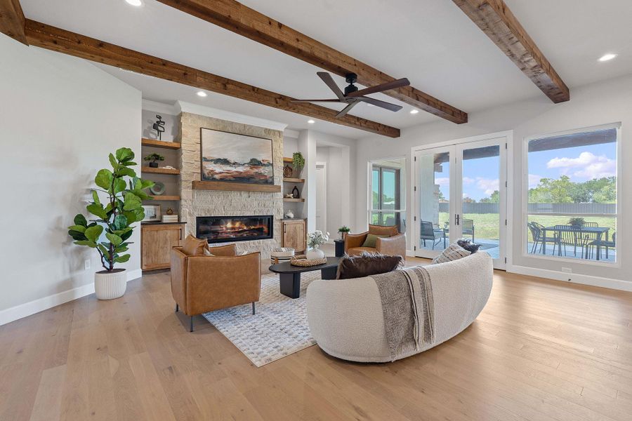 Living area featuring a large fireplace, beam ceiling, ceiling fan, plenty of natural light, and light wood finished floors