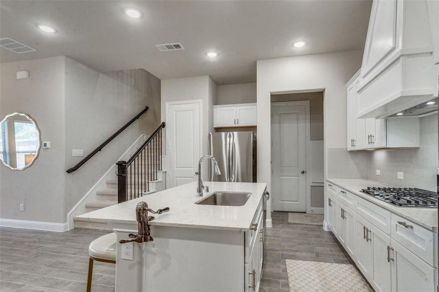 Kitchen with custom range hood, stainless steel appliances, a center island with sink, tasteful backsplash, and sink