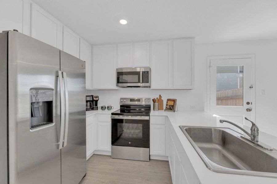 Open kitchen with stainless steel appliances, white cabinetry, recessed lighting, light vinyl floors, and light stone countertops