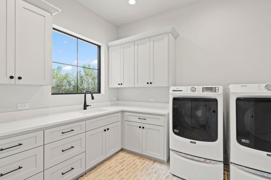 Laundry area with brick flooring, washing machine and clothes dryer, cabinet space, and utility sink.