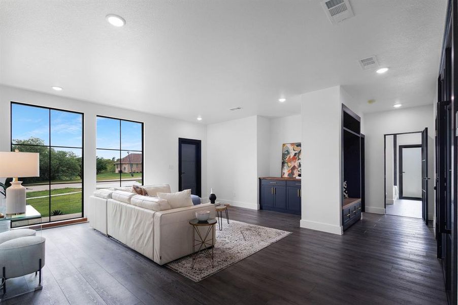 Spacious living area featuring large picture windows, recessed lighting, dark wood-finish flooring, a built-in console with lower cabinetry, and a built-in entryway bench with storage Spacious living area featuring large picture windows, recessed lighting, dark wood-finish flooring, a built-in console with lower cabinetry, and a built-in entryway bench with storage