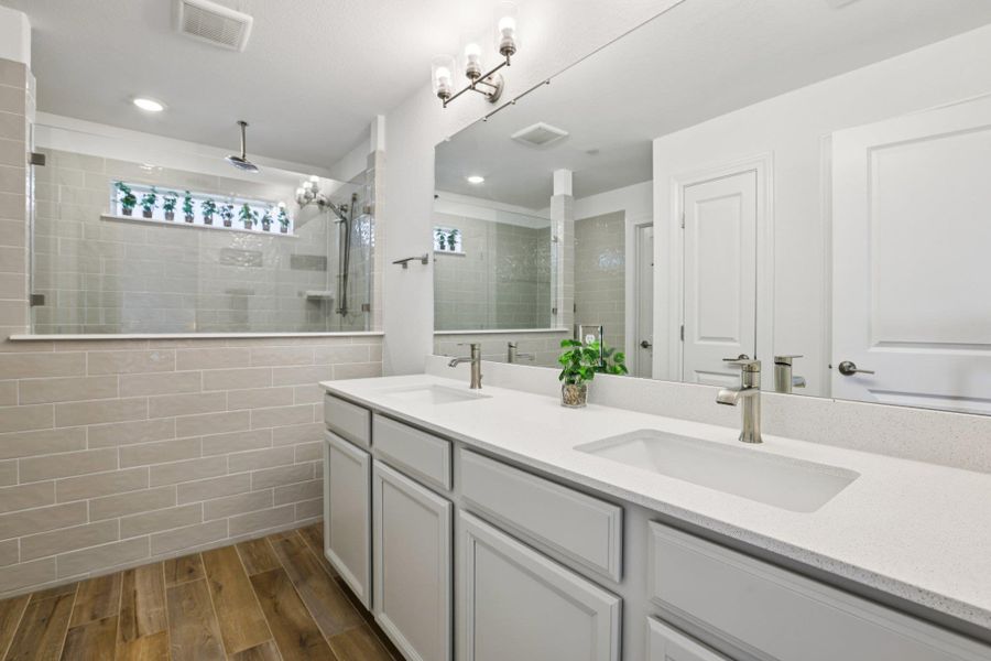 Well-appointed bathroom featuring a double vanity with white countertops, a large mirror, and wood-look tile flooring