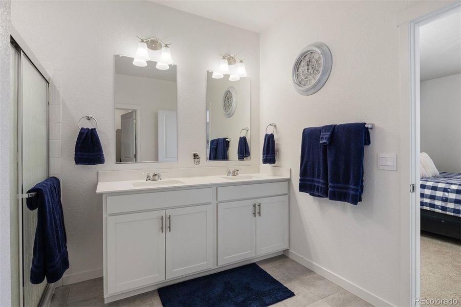 Ensuite with dual sinks, quartz counters, white cabinetry, and a walk-in shower accented by clean tile lines.