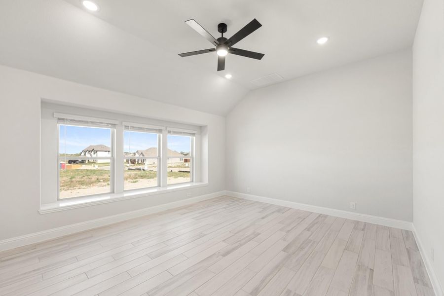 Empty bedroom with vaulted ceiling, black ceiling fan, light wood floors, and triple windows overlooking neighborhood