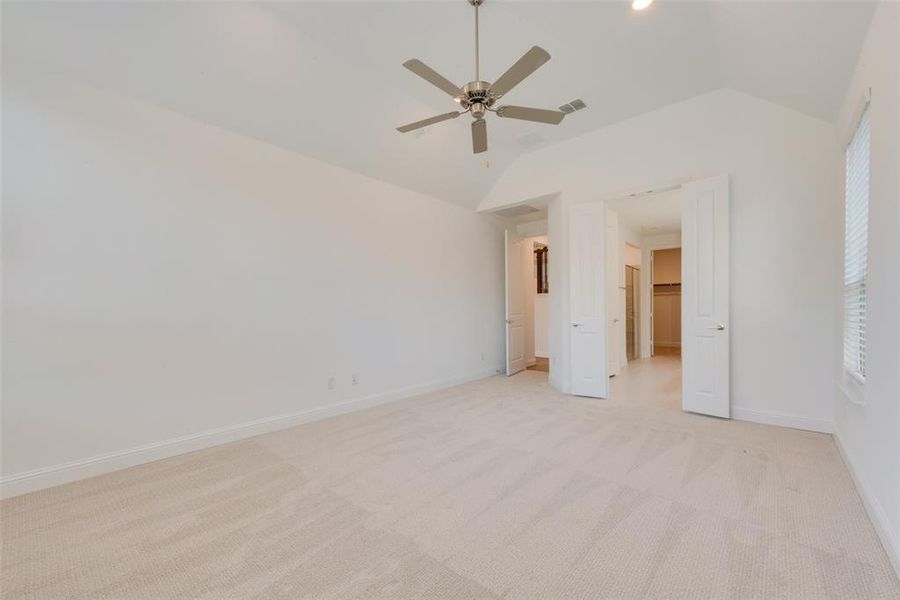 Unfurnished bedroom with light colored carpet, ceiling fan, and vaulted ceiling