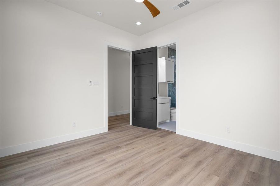 The room features light wood-style flooring, white walls with white baseboards, and a dark paneled door The room features light wood-style flooring, white walls with white baseboards, and a dark paneled door