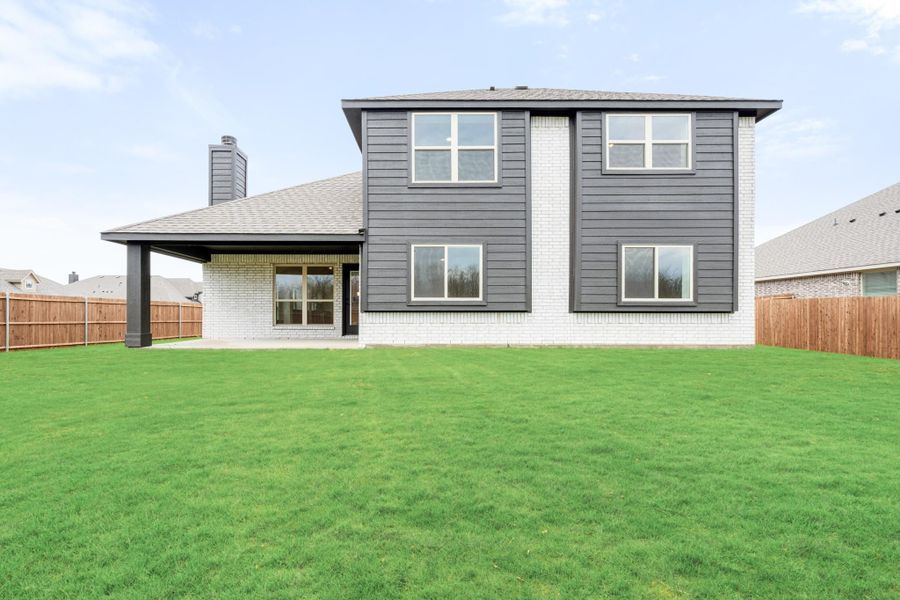 Two-story home rear view with dark gray siding, white brick, covered patio, and large fenced backyard