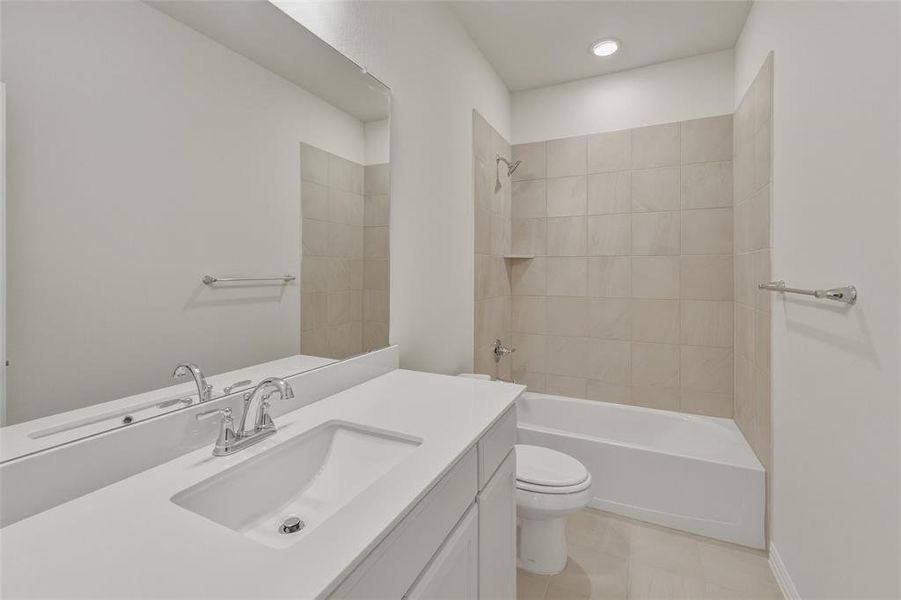 Bathroom featuring a white vanity with an integrated sink, polished chrome faucet, a large frameless mirror, and a tiled shower/tub combination with a built-in shelf Bathroom featuring a white vanity with an integrated sink, polished chrome faucet, a large frameless mirror, and a tiled shower/tub combination with a built-in shelf