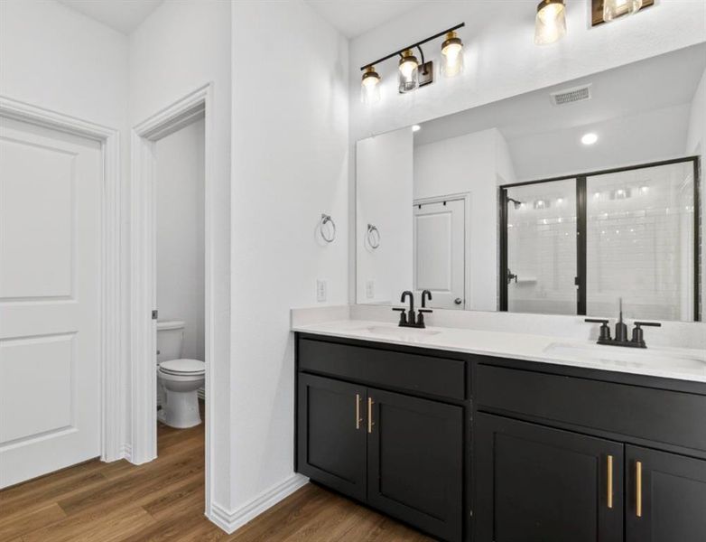 Bathroom featuring double vanity, dark wood-style flooring, and a stall shower